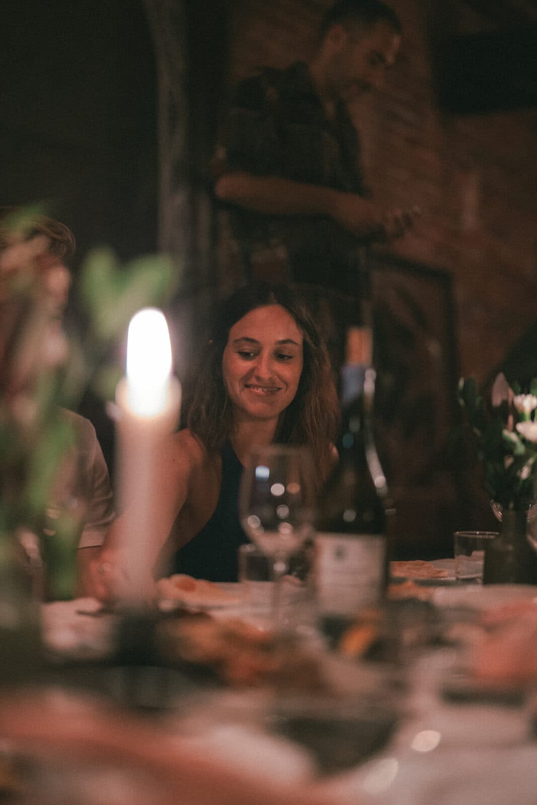A guest smiling at the long table at TEJÁ, a candle and a bottle of wine in front of her.