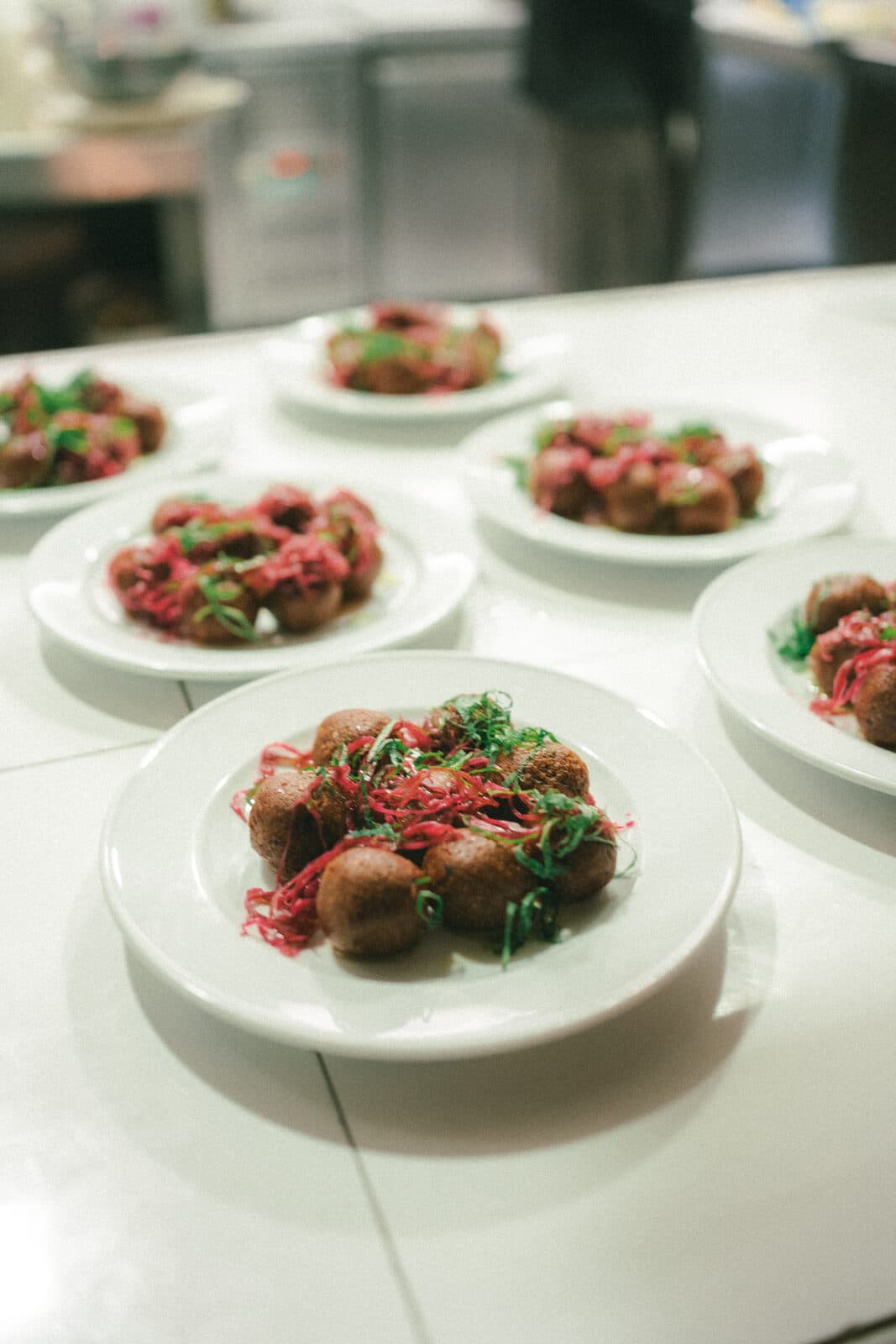 Plates of meatballs with herbs lined up on the pass in the kitchen at TEJÁ.