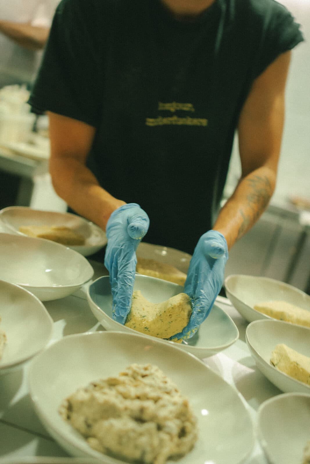 A cook in blue gloves plating dishes by hand in the kitchen at TEJÁ.