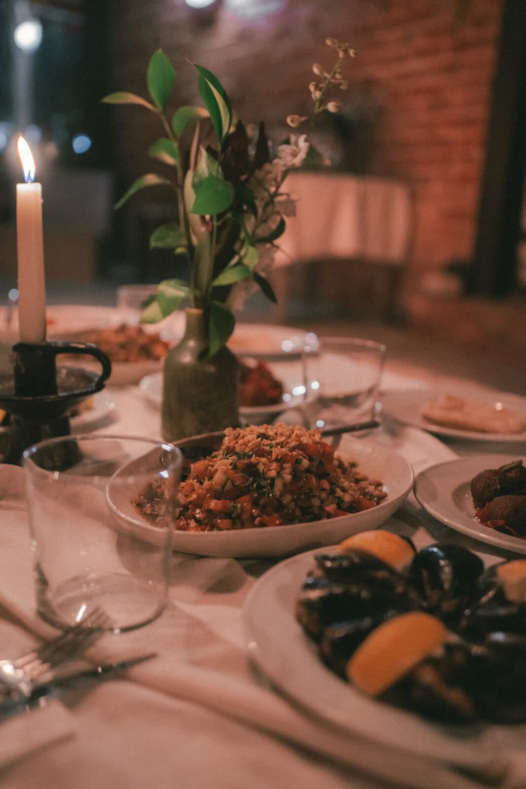 Dishes and mussels on the long table at TEJÁ, a candle and a vase of leaves beside them.