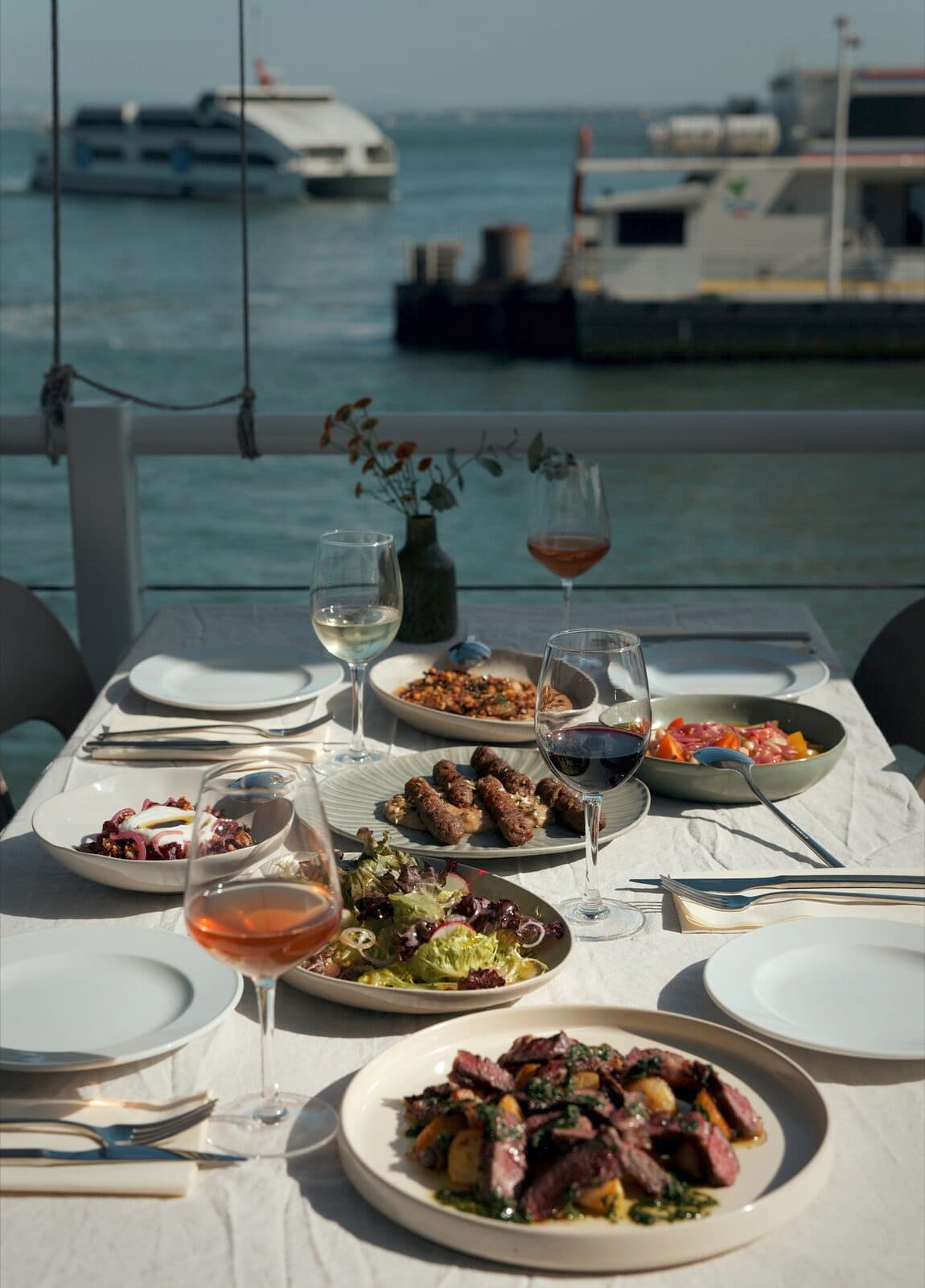 A table laid on the terrace with dishes and glasses, ferries on the river behind.