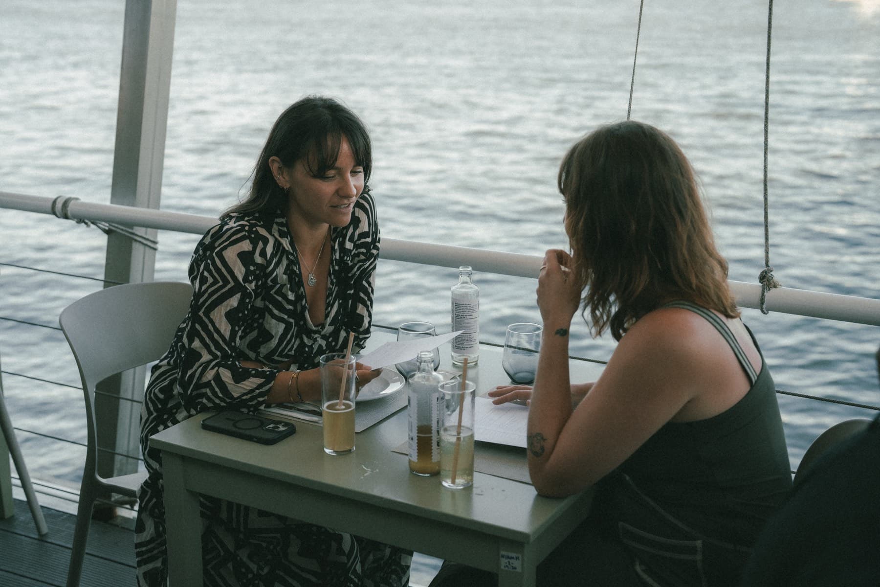 Two women talking at a table on the terrace, the river behind them.