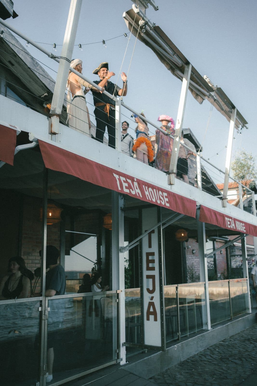 The front of TEJÁ House from the quay, people on the balcony above the sign.
