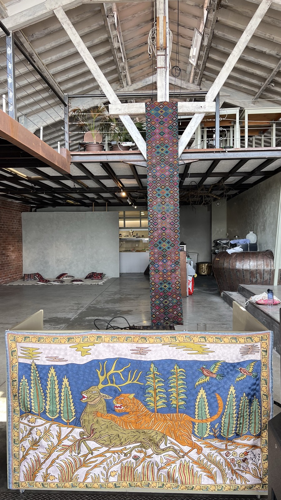 the hall at teja with a kilim-wrapped column and a painted folk tapestry of a deer and a tiger