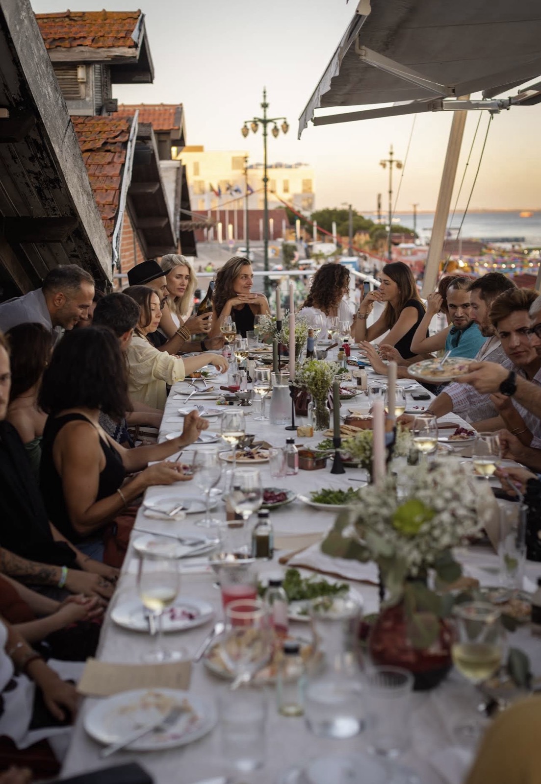 a long table on the terrace at teja at golden hour, people eating with the boats behind them